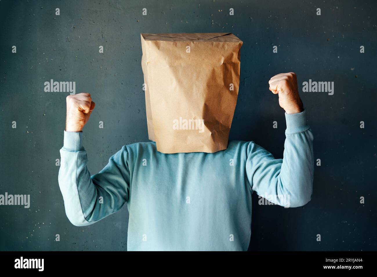 Uomo felice con un sacchetto di carta in testa che celebra il suo successo con il gesto del vincitore Foto Stock