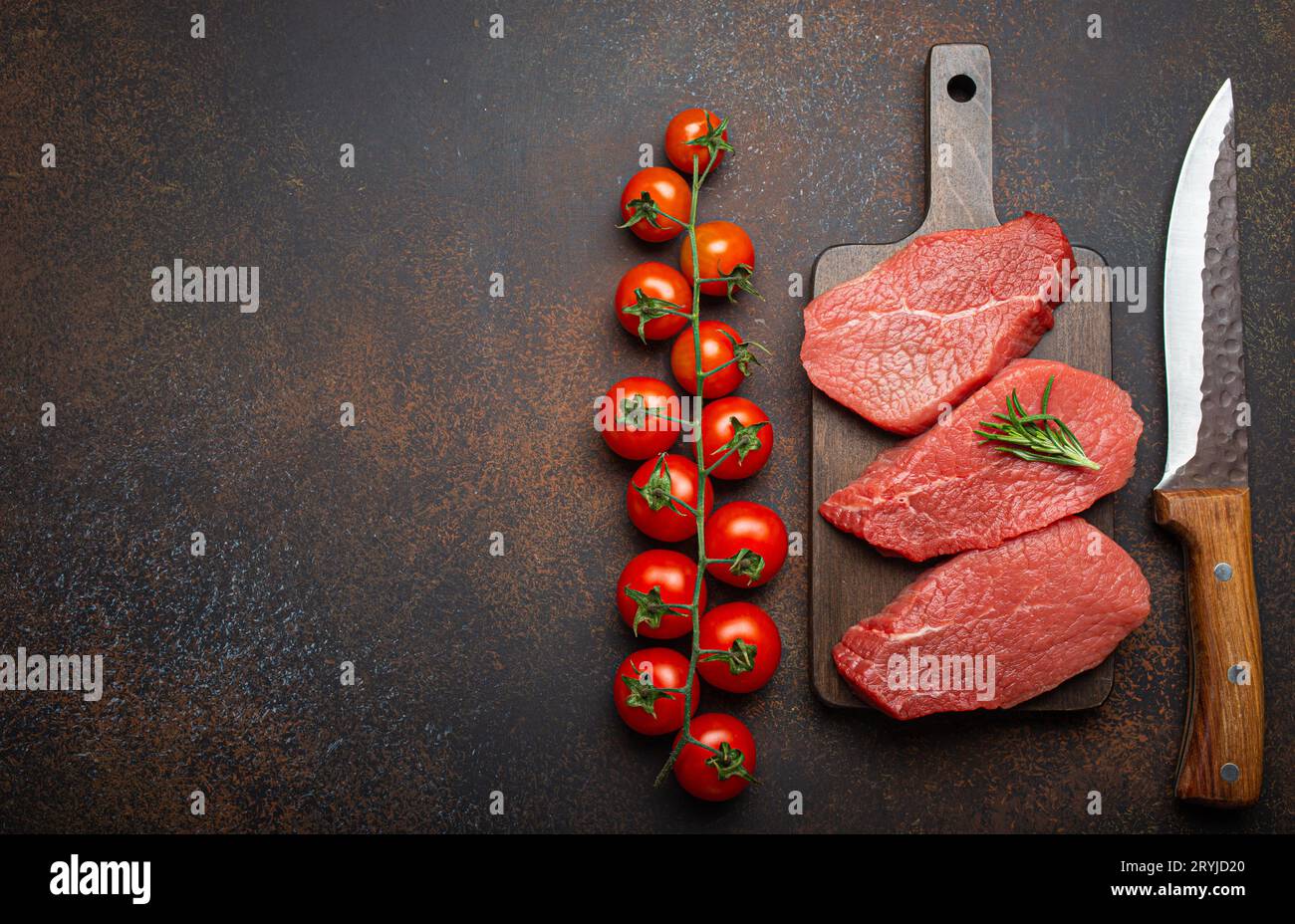 Tre bistecche di manzo crude su tagliere di legno con rosmarino su tagliere di legno con pomodoro ciliegia Foto Stock