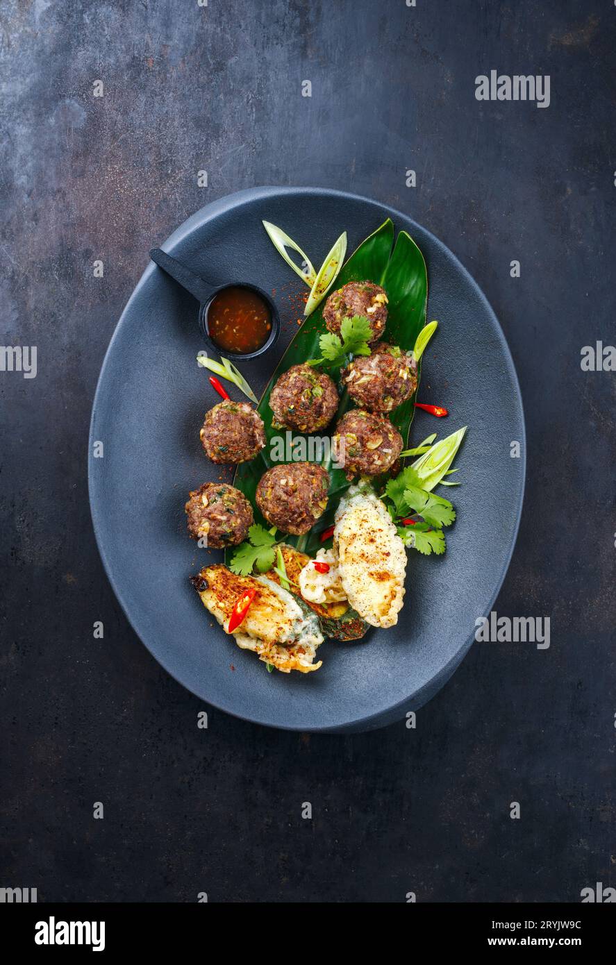 Tradizionali polpette di carne asiatiche servite con verdure tempura e salsa piccante al peperoncino come vista dall'alto su un piatto di design Foto Stock