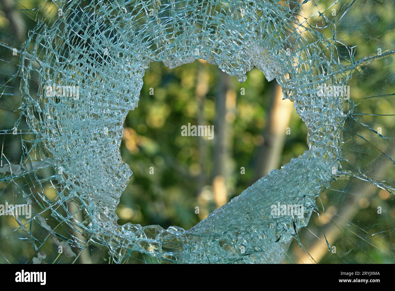 Un foro nel vetro o nella finestra. Finestra rotta e forata che si affaccia sullo sfondo verde. Un buco da un guscio o proiettile nel vetro di una casa Foto Stock