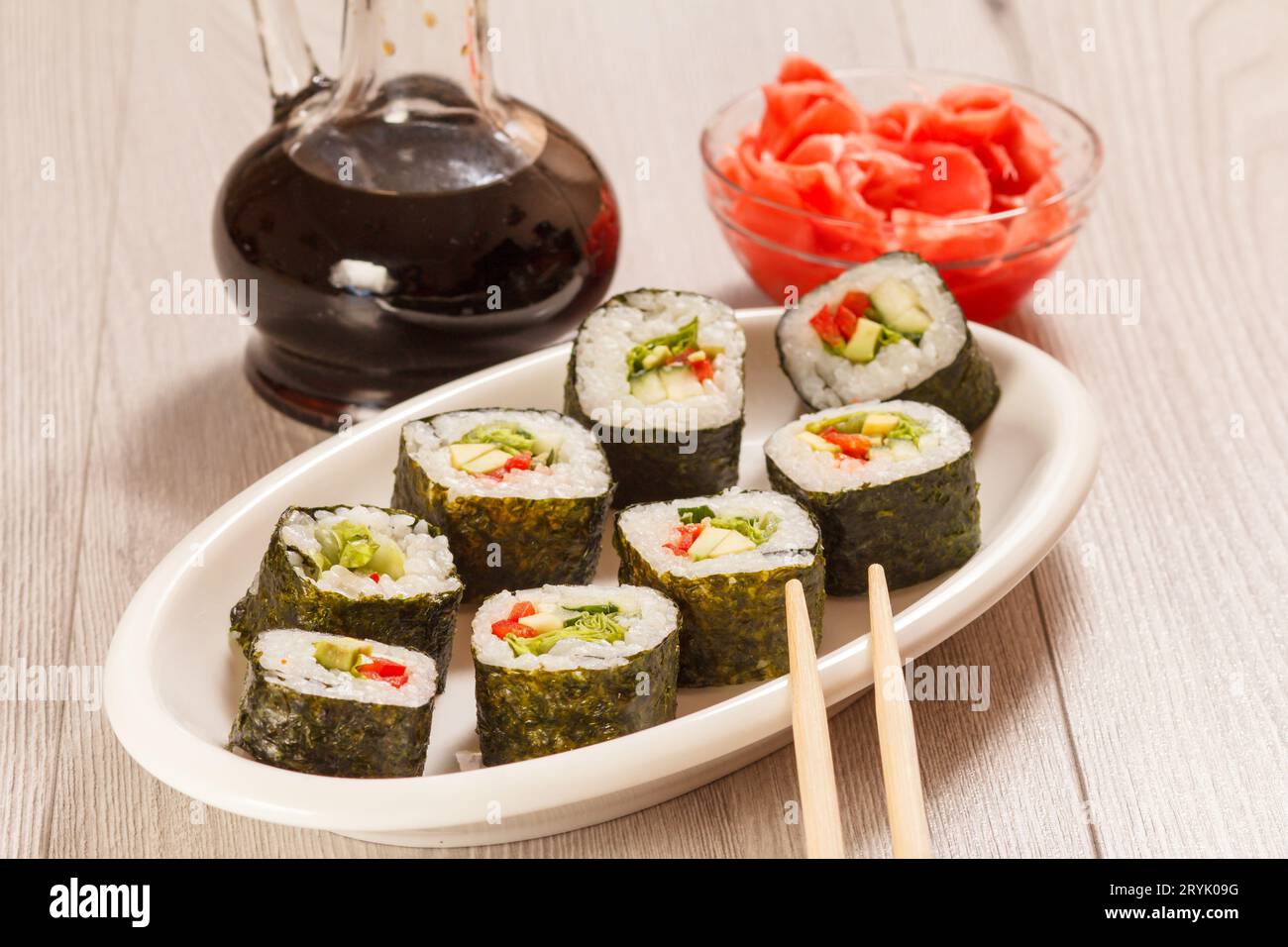 Involtini di sushi con riso, verdure e frutti di mare su piatto con bottiglia di salsa di soia. Foto Stock