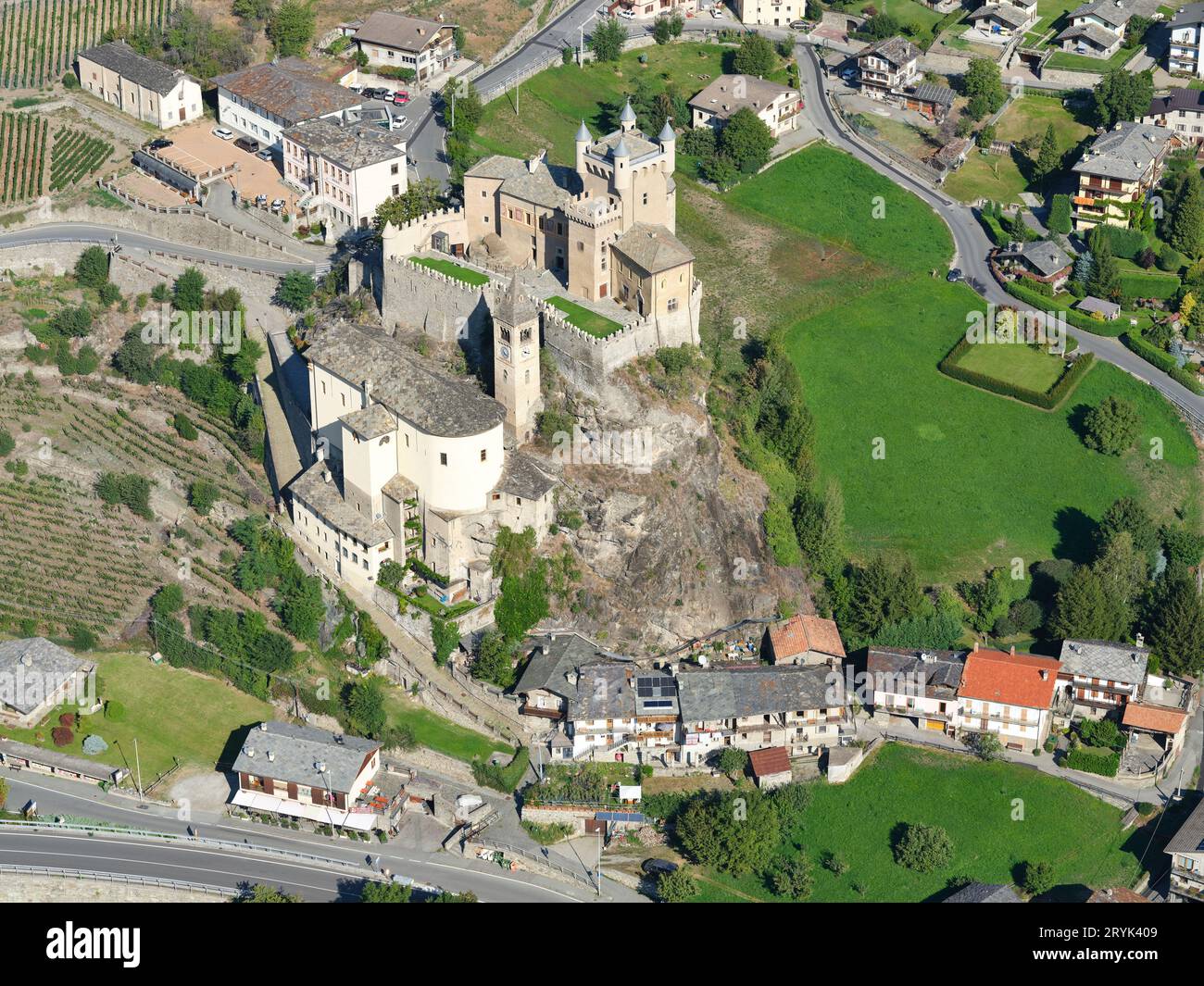 VISTA AEREA. Castello di Saint-Pierre e chiesa parrocchiale su uno sperone roccioso. Saint-Pierre, Valle d'Aosta, Italia. Foto Stock