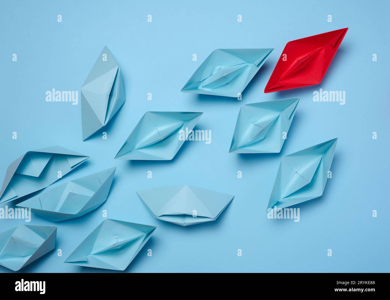 Un gruppo di barche di carta blu segue il bianco su uno sfondo azzurro. Forte concetto di leader, manipolazione di massa. Foto Stock