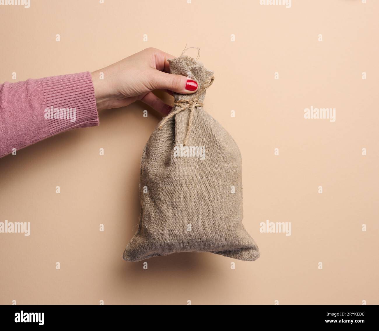 Una mano della donna tiene una borsa di tela su uno sfondo beige, il concetto di un sussidio, aiuto Foto Stock