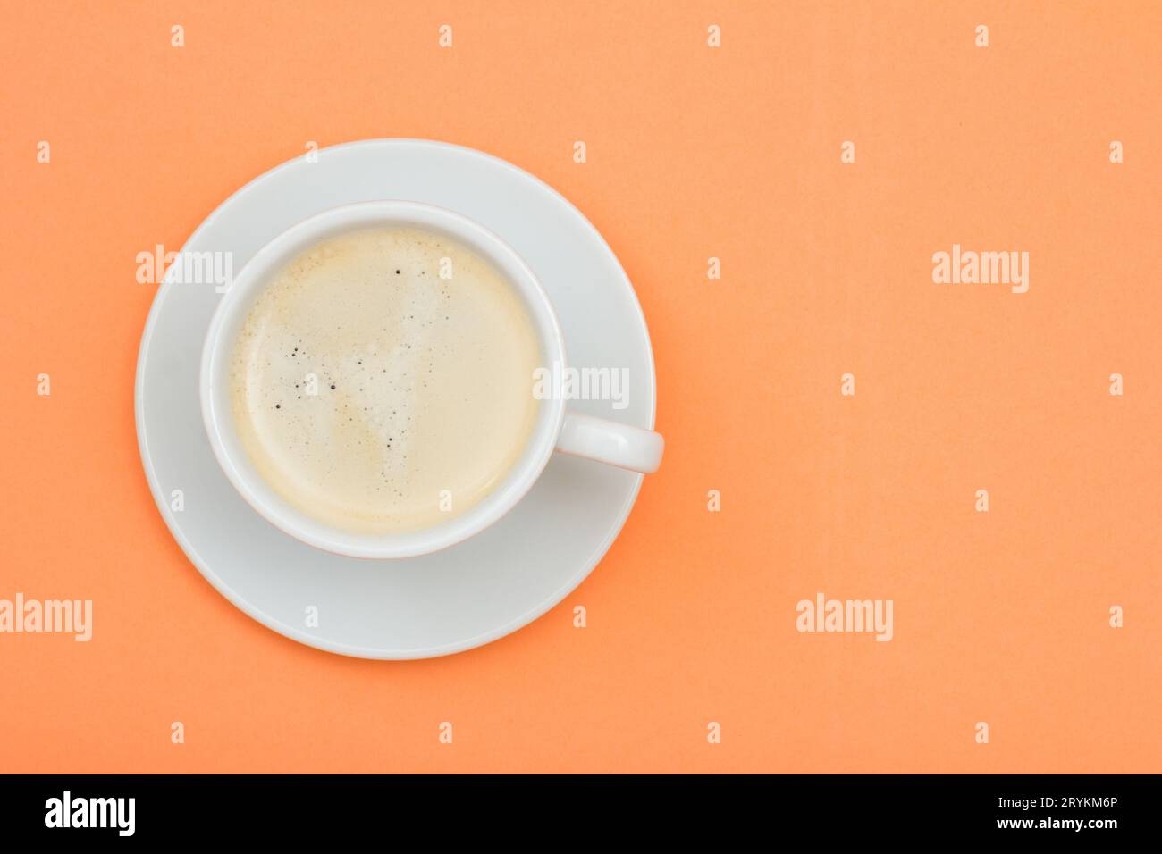 Tazza di caffè nero in porcellana bianca su un piattino sullo sfondo di colore pesca Foto Stock