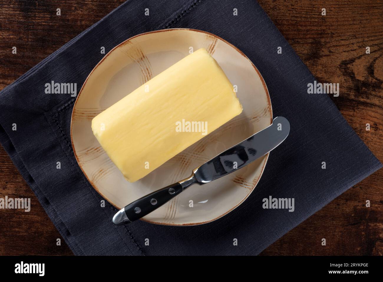 Un blocco di burro con un coltello su un piatto e un getto di latte piatto Foto Stock