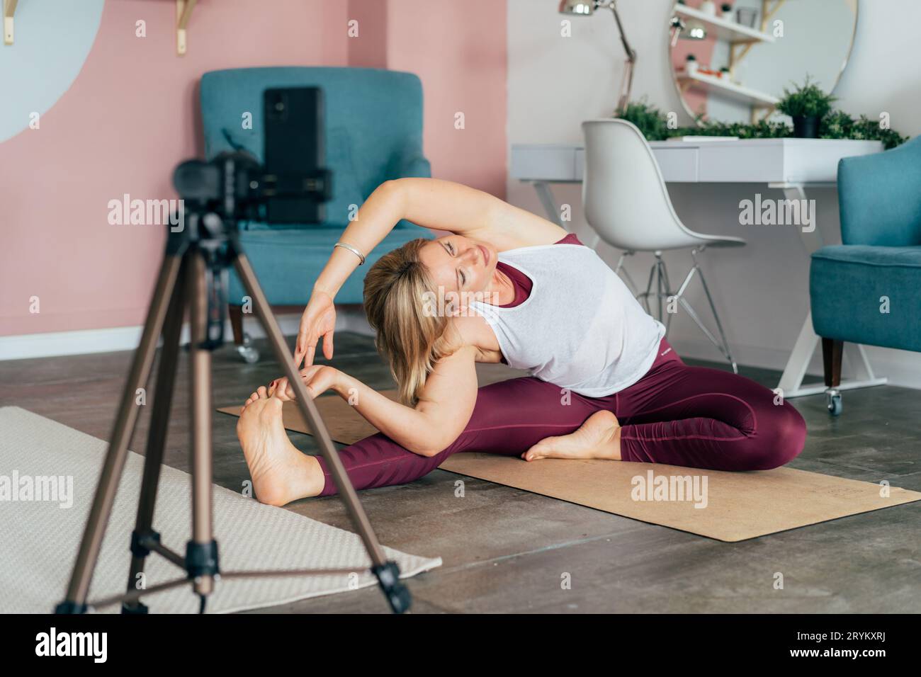 Una donna che indossa abbigliamento sportivo lavora a casa su un tappetino davanti a un telefono cellulare. Formazione online Foto Stock