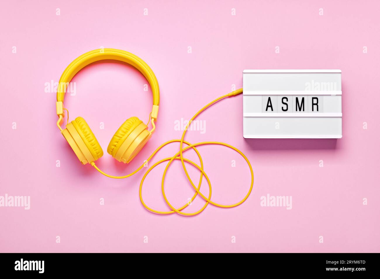 Cuffie gialle e lightbox con lettere ASMR su sfondo rosa. ASMR per un'atmosfera rilassante, piatto Foto Stock