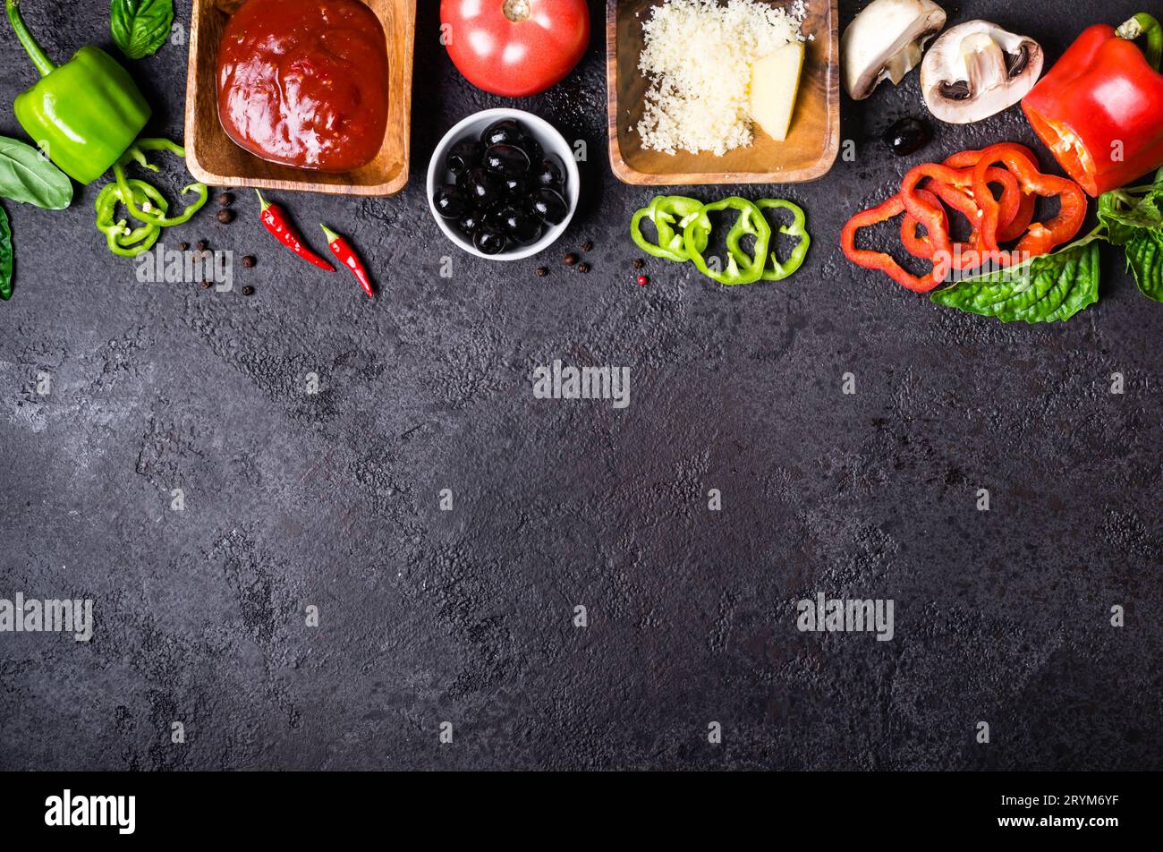 Ingredienti per cucinare la pizza. Salsa di pomodoro, pepe dolce, olive, formaggio, funghi e basilico su sfondo nero. Foto Stock