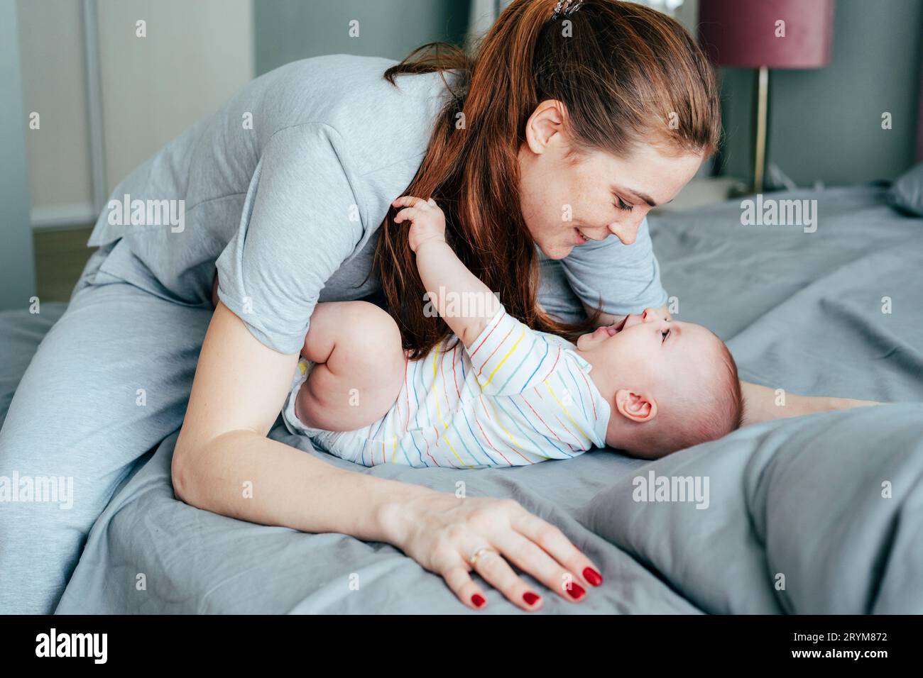 La mamma felice coccola il suo innocente adorabile neonato al mattino in camera da letto. Foto Stock