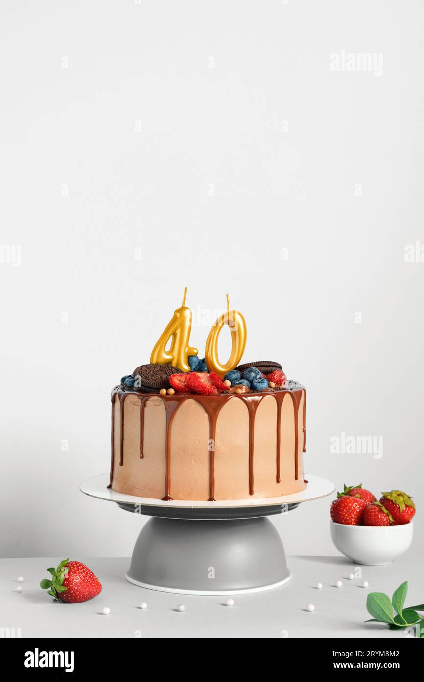 Torta di compleanno al cioccolato con frutti di bosco, biscotti e quaranta candele dorate su sfondo bianco, spazio copia Foto Stock