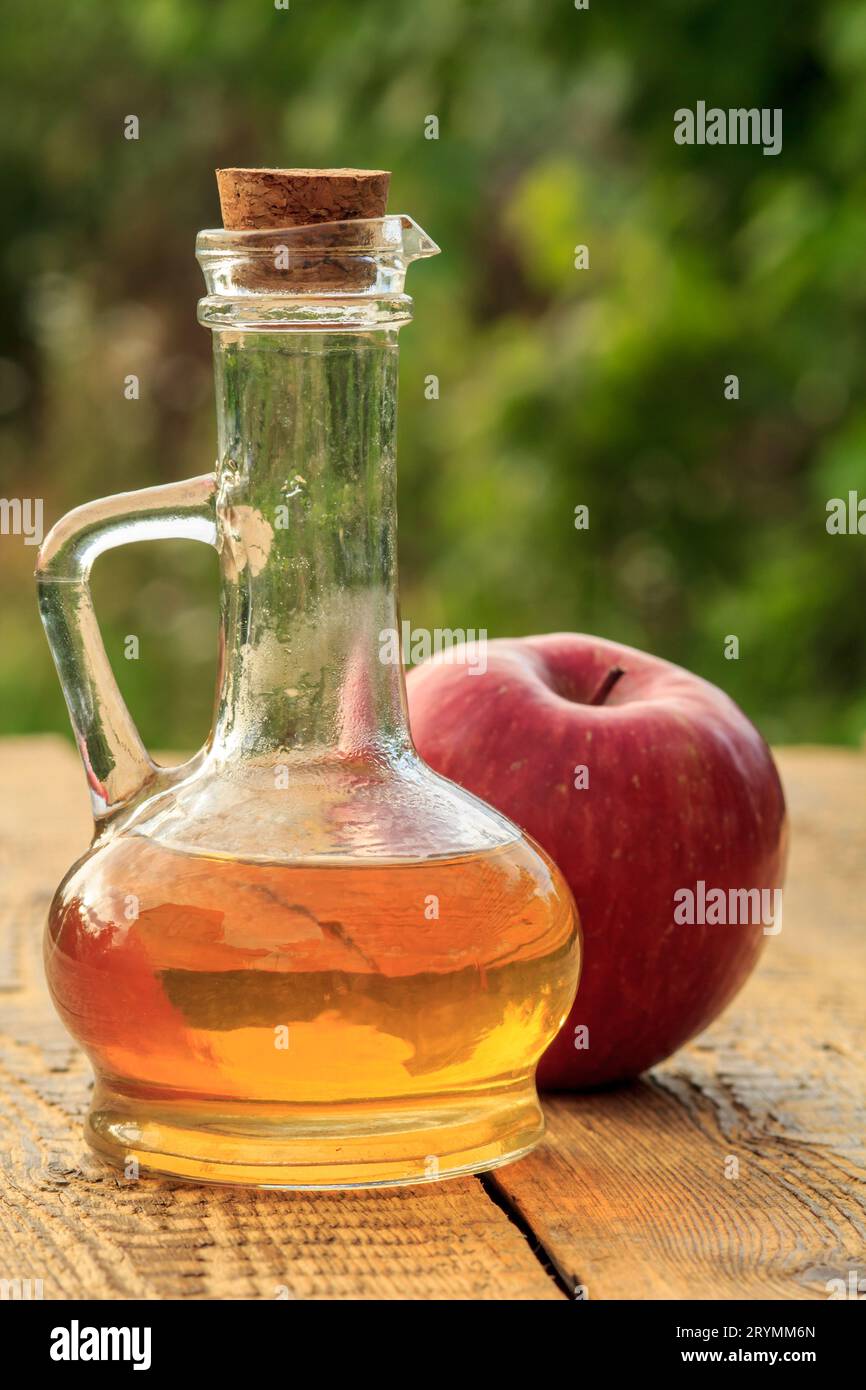 Aceto di mele nella bottiglia di vetro e una mela rossa fresca sulle tavole di legno Foto Stock