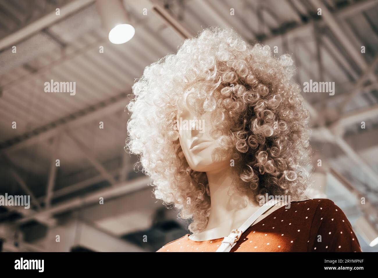 Il manichino in parrucche ricci sta nel negozio di abbigliamento. Shopping, moda e sfondo pubblicitario Foto Stock