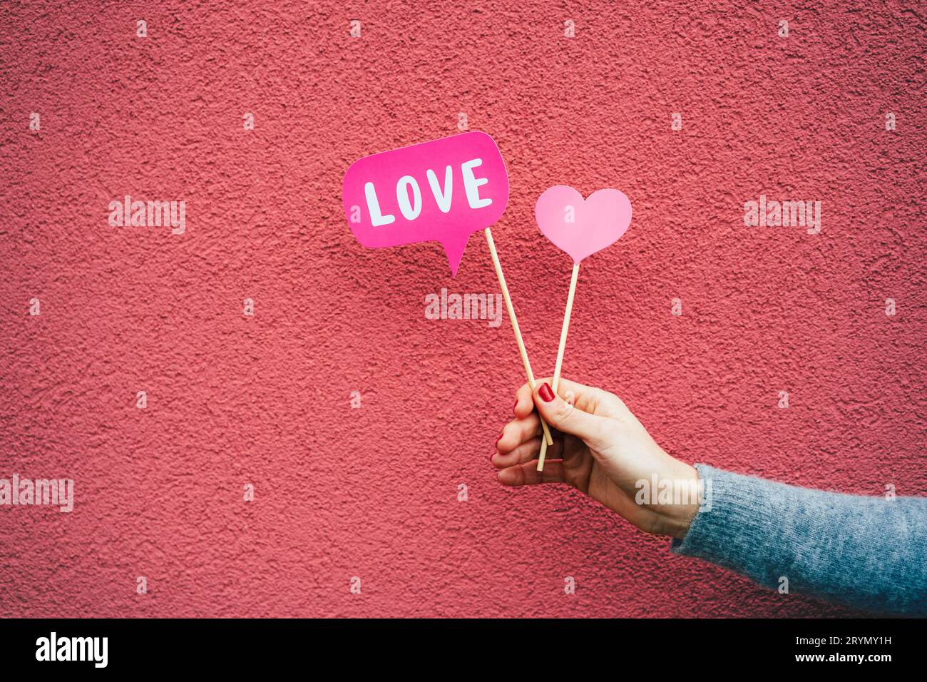 In una mano femminile, carta bandiere di amore su bastoni su uno sfondo rosa. Foto Stock