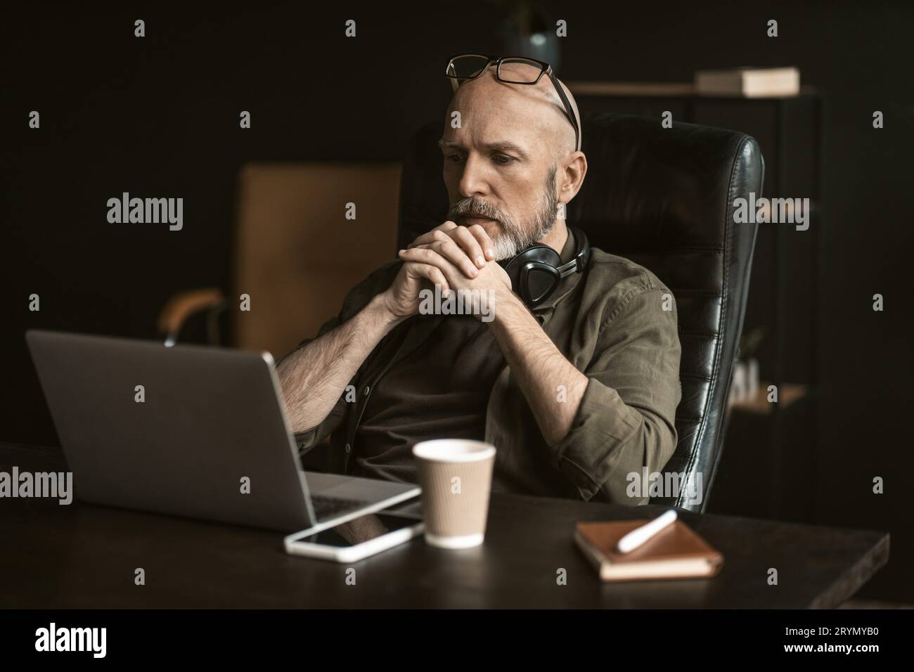 Lavoratore anziano dedicato in un ufficio loft. Con un'espressione sconcertata sul suo viso, siede attento di fronte a un comp Foto Stock