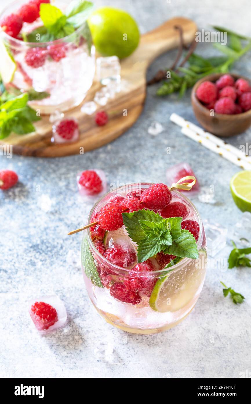 Cocktail seltzer duro con lamponi e lime su un tavolo in pietra grigia. Foto Stock