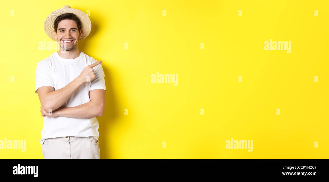 Giovane turista maschile che punta il dito a destra, sorridendo e mostrando pubblicità, concetto di turismo e stile di vita, sfondo giallo Foto Stock