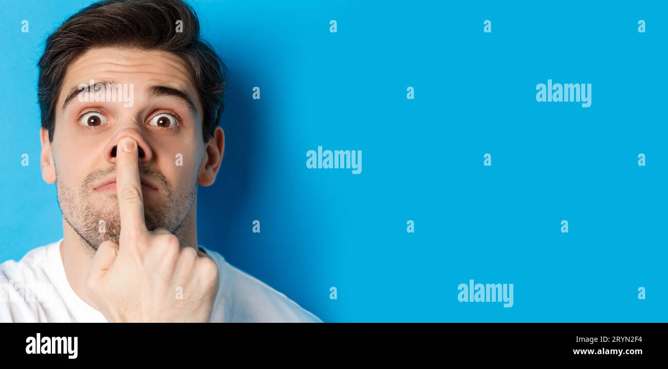 Headshot di un ragazzo caucasico che fa espressioni divertenti, in piedi su sfondo blu Foto Stock