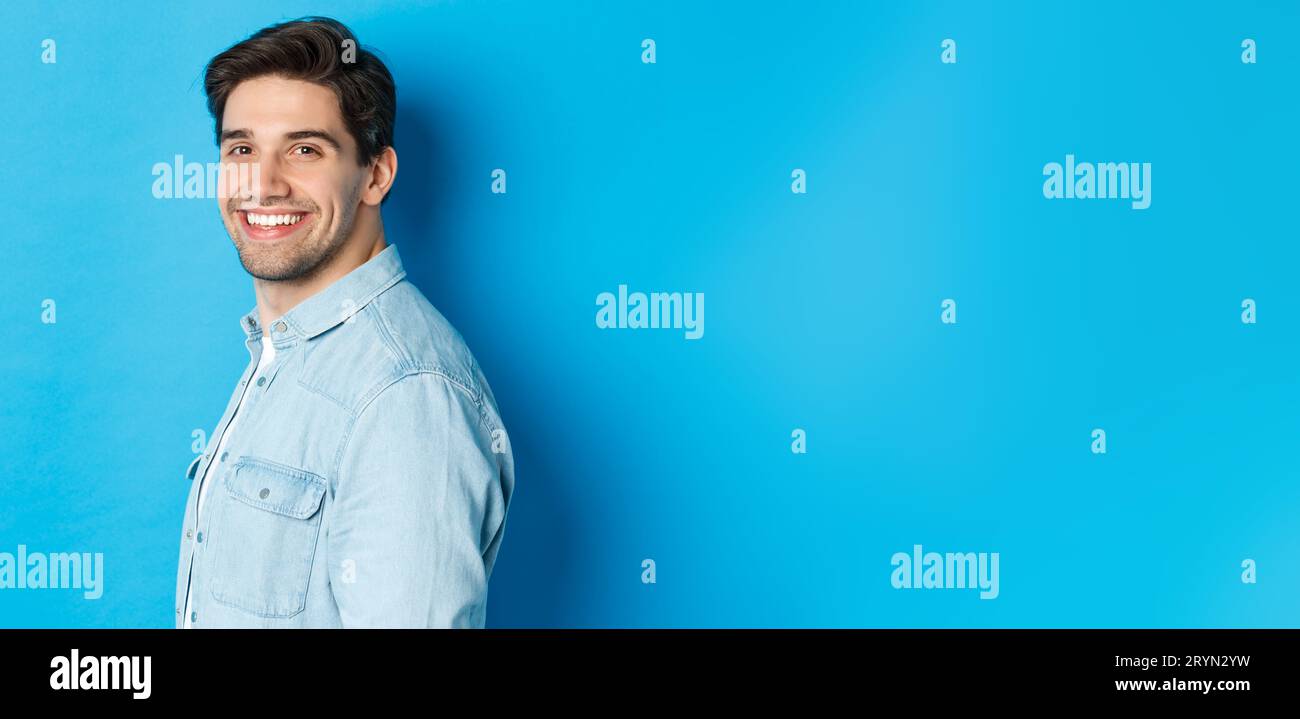 Un ragazzo bello e sicuro si dirige verso la telecamera, sorridendo felice, in piedi su sfondo blu Foto Stock
