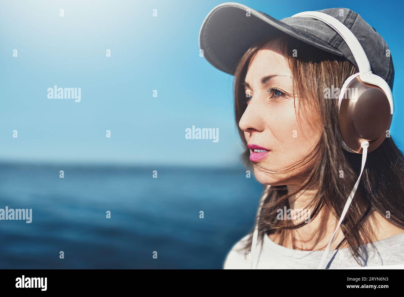 Ritratto ravvicinato di una donna con occhiali da sole che indossa un berretto che ama la musica sullo sfondo del mare. Concetto di musica. Foto Stock