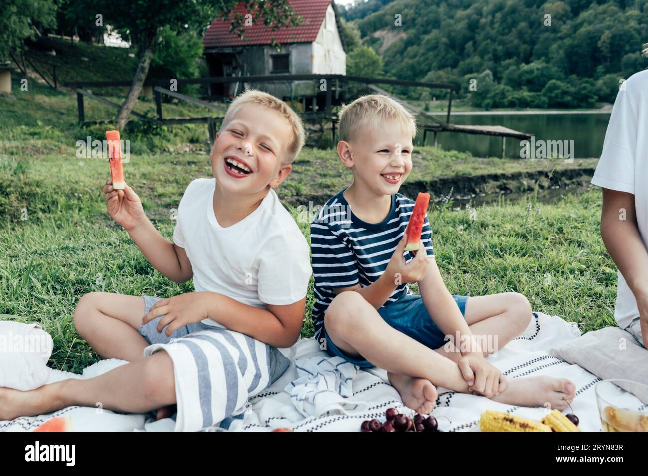 Due ragazzi preadolescenti ridono di gioia al picnic. I bambini tengono pezzi di anguria Foto Stock