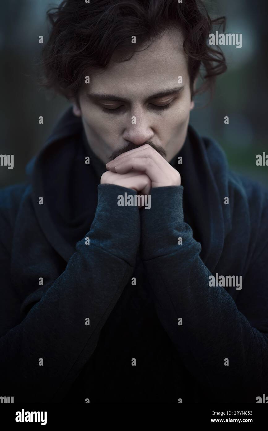 Bel giovane uomo riccio sente fede e speranza. si bacia le mani Foto Stock