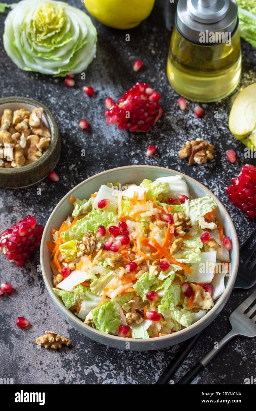 Insalata di cavolo cinese con dieta autunnale verdure fresche, carote, mela, noci e melograno con condimento vinaigrette su un tavolo di pietra scuro. Foto Stock