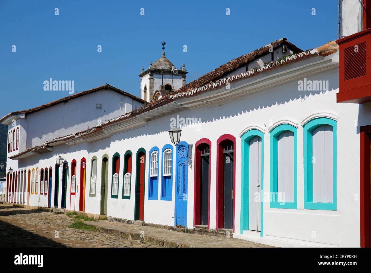 Facciate tipiche delle case al sole con porte e finestre colorate, nel campanile della chiesa sullo sfondo Foto Stock