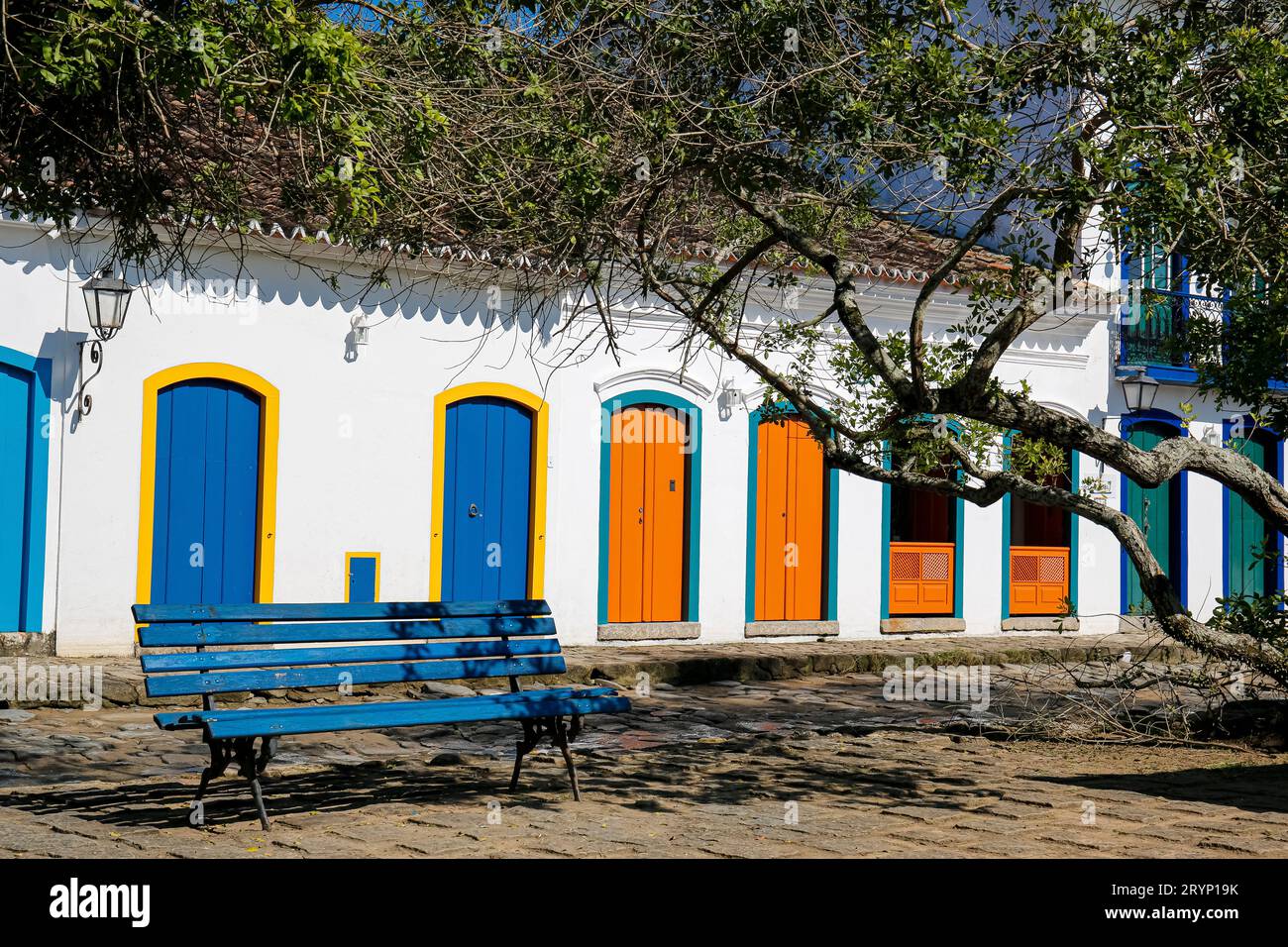 Vista delle facciate delle case coloniali con colorate porte in legno al sole con panca blu e reggiseno ad albero Foto Stock