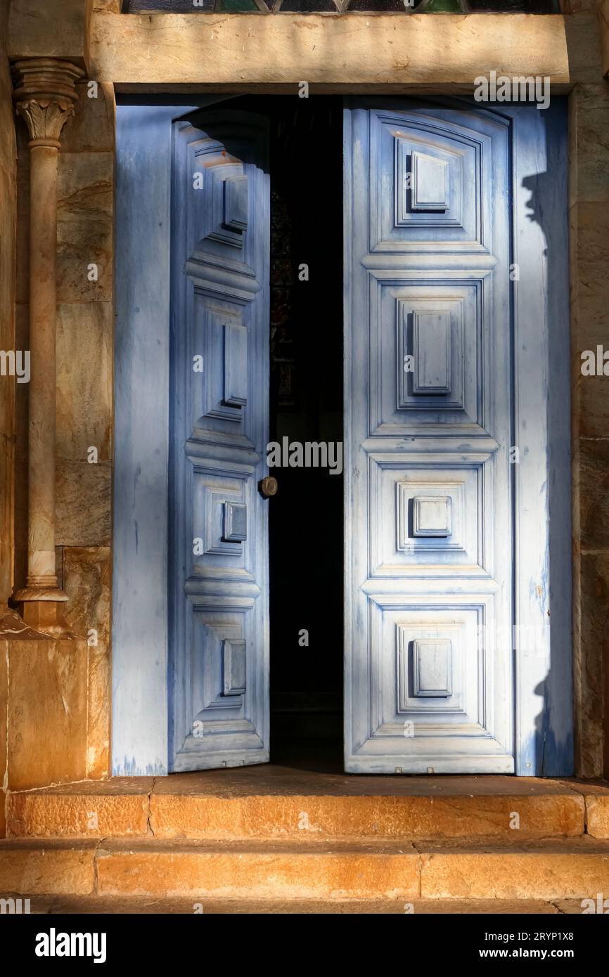Porta d'ingresso parzialmente aperta blu con ornamenti in calda luce pomeridiana, Catas Altas, Minas Gerais, BR Foto Stock