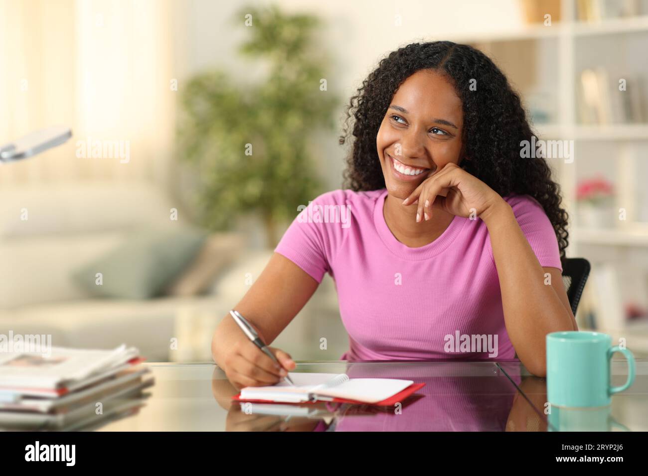 Felice donna nera che scrive all'ordine del giorno sognando di guardare da parte a casa Foto Stock
