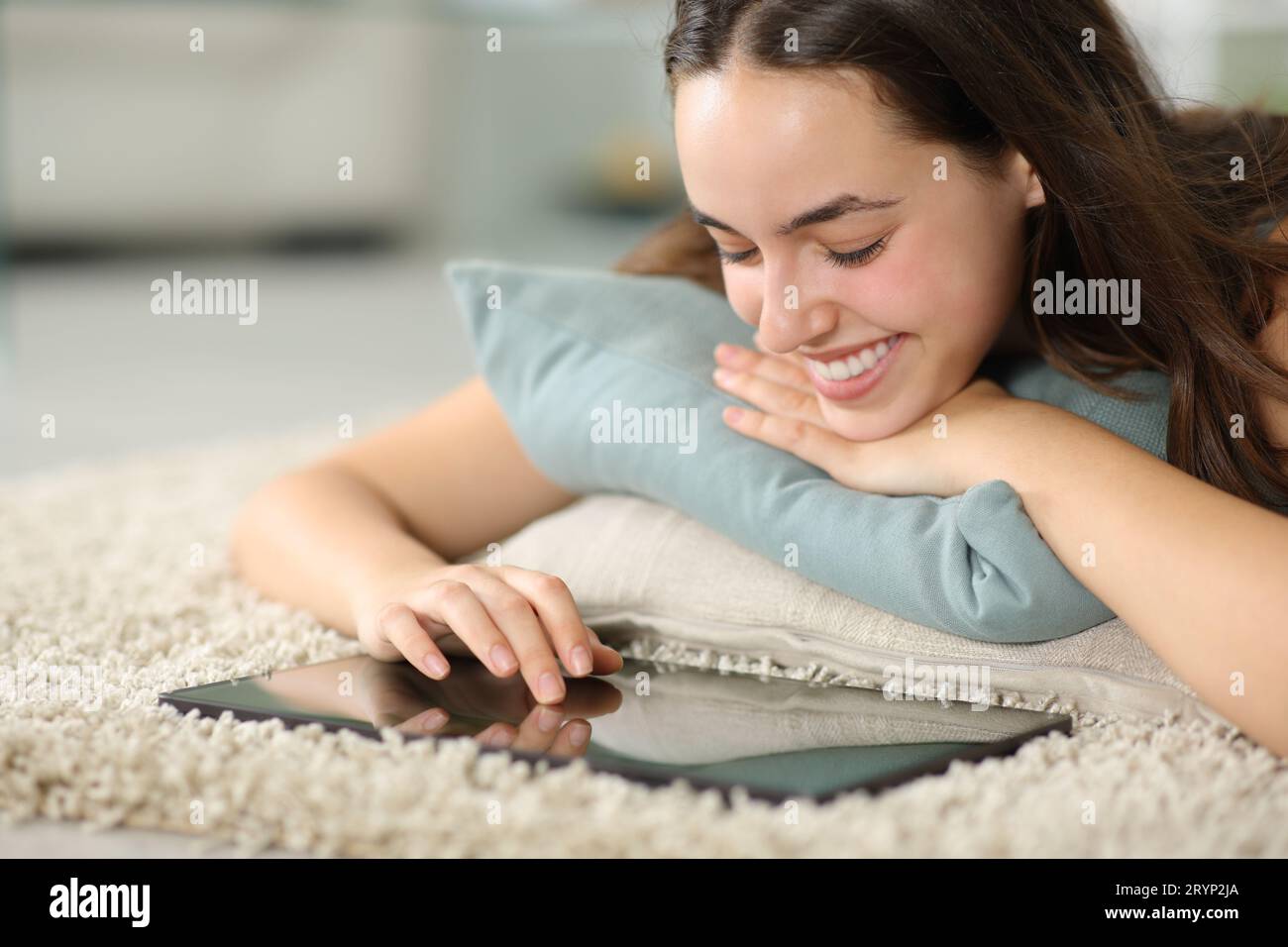 Donna felice che usa un tablet sdraiato sul tappeto a casa Foto Stock