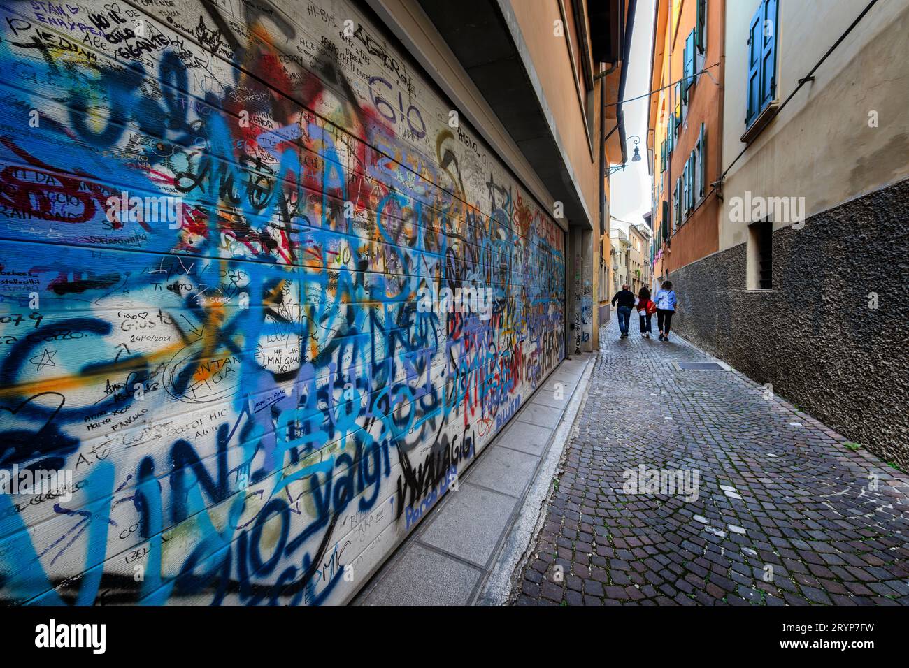 Cartellini e scritte su una porta del garage che si affaccia su uno stretto vicolo italiano. Vandalismo urbano. Foto Stock