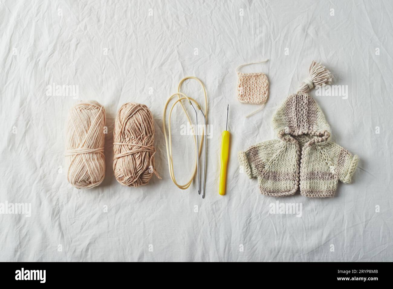 Maglioni e fili piccoli lavorati a maglia a mano su sfondo chiaro. Foto Stock