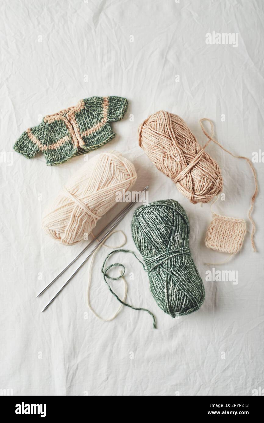 Maglioni e fili piccoli lavorati a maglia a mano su sfondo chiaro. Foto Stock