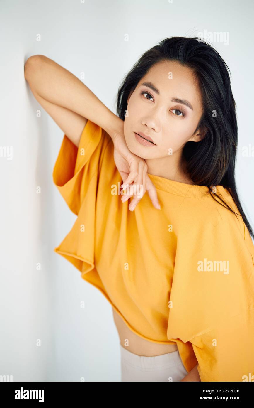 Bella sensuale donna asiatica in maglietta gialla brillante in posa su sfondo bianco studio. Bellezza femminile Foto Stock