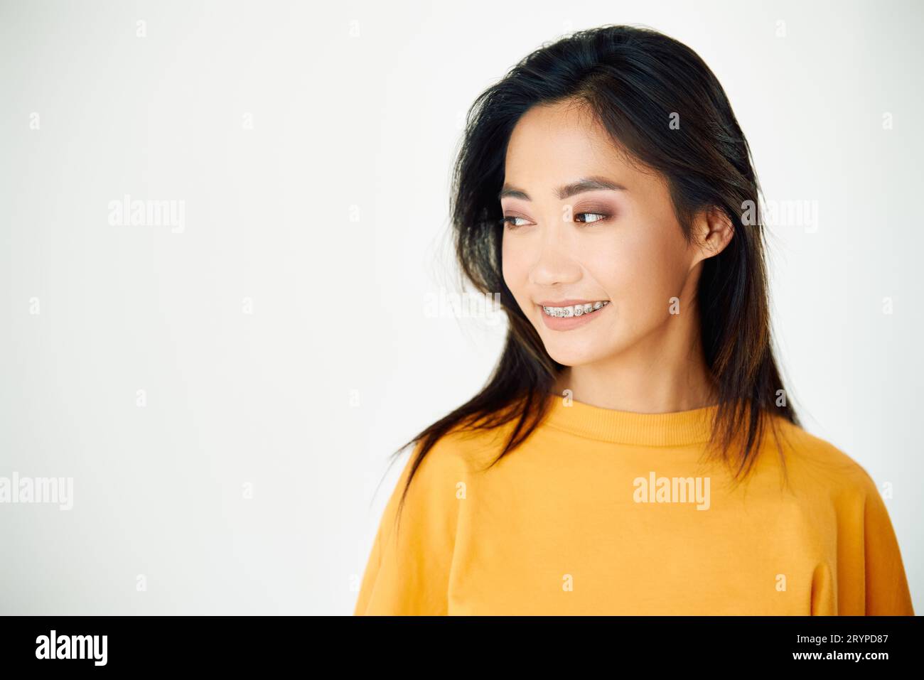 Giovane donna asiatica sorridente con apparecchio che guarda da parte per copiare spazio su sfondo bianco dello studio Foto Stock
