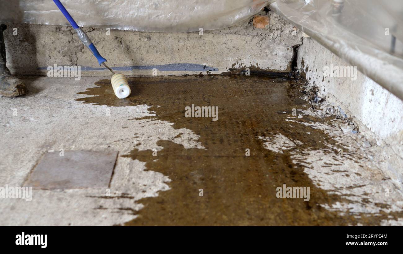 Processo di adescamento del pavimento. Un lavoratore applica un primer su un pavimento di cemento prima di posare un pavimento autolivellante. Primer per pavimenti in calcestruzzo per rafforzare Foto Stock