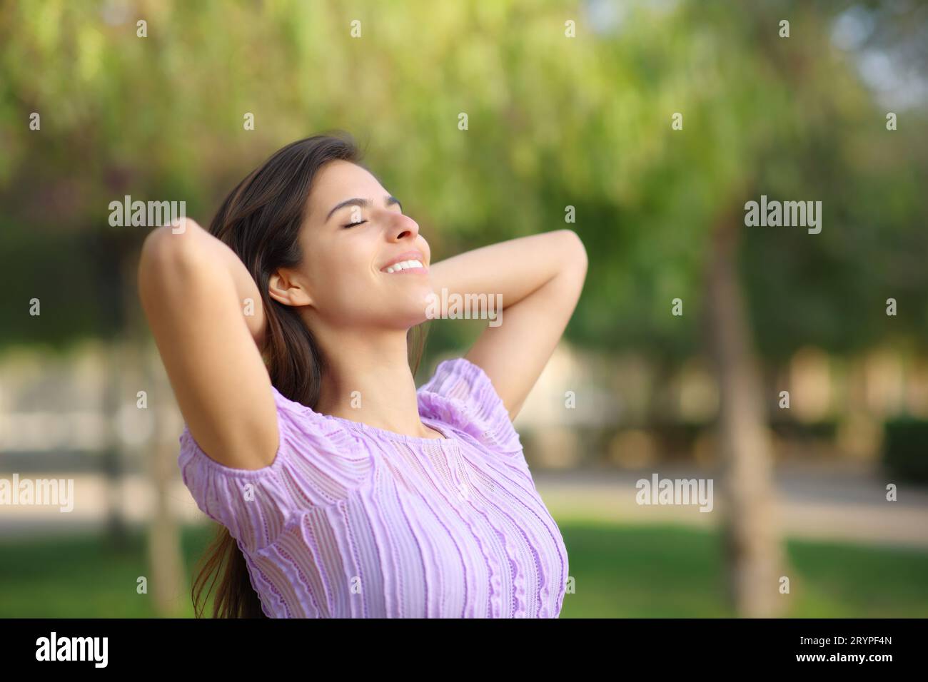 Donna felice che si rilassa con le mani sulla testa in un parco da sola Foto Stock