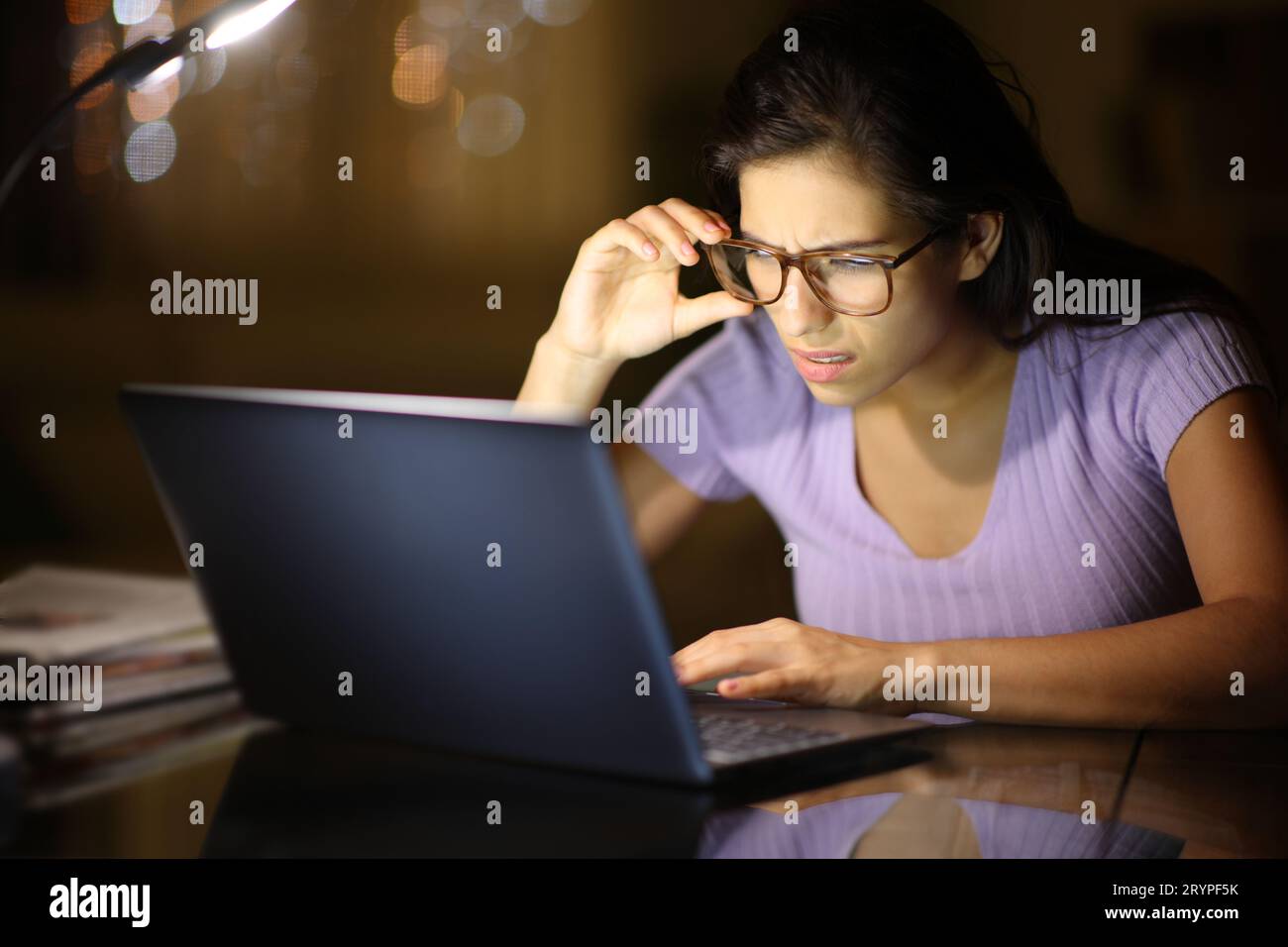 Donna che usa gli occhiali da vista che si vede con un notebook di notte a casa Foto Stock