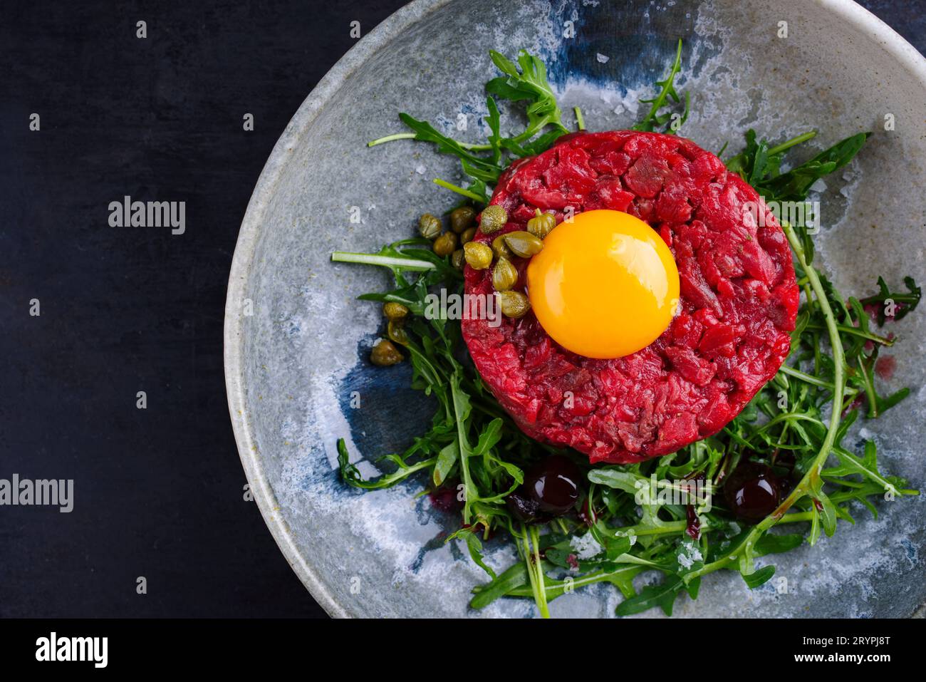 Tartaro gourmet di stile moderno crudo di filetto di manzo con uovo, rucola e capperi servito come vista dall'alto su un piatto di design con spazio per la copia a destra Foto Stock