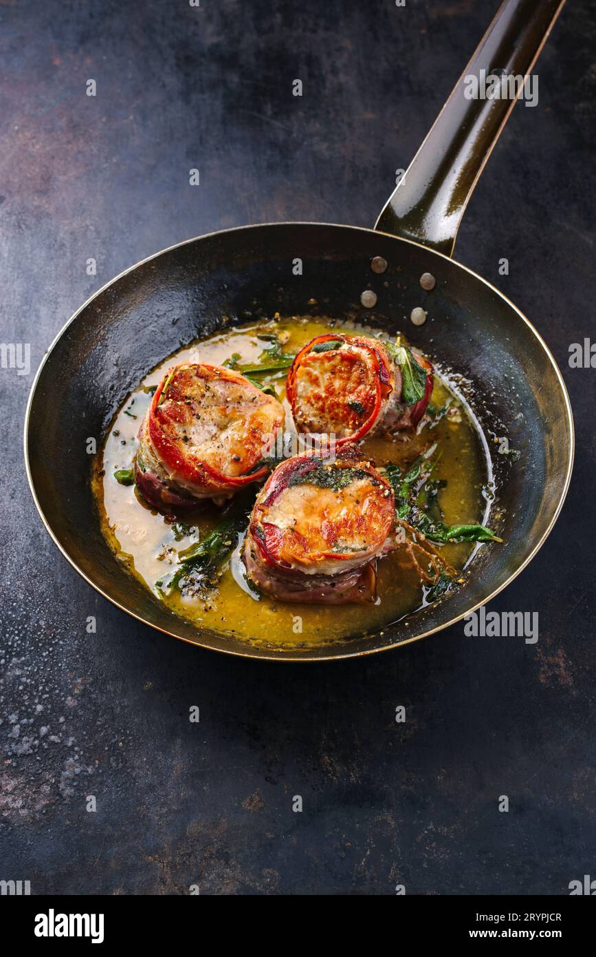 Tradizionali medaglioni di filetto di vitello arrosto con rivestimento di pancetta e foglie di salvia in salsa di burro serviti da vicino su un battuto rustico Foto Stock