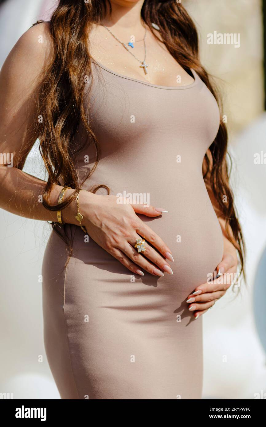 Una donna incinta in posa mozzafiato, che tiene la pancia e indossa gioielli Foto Stock