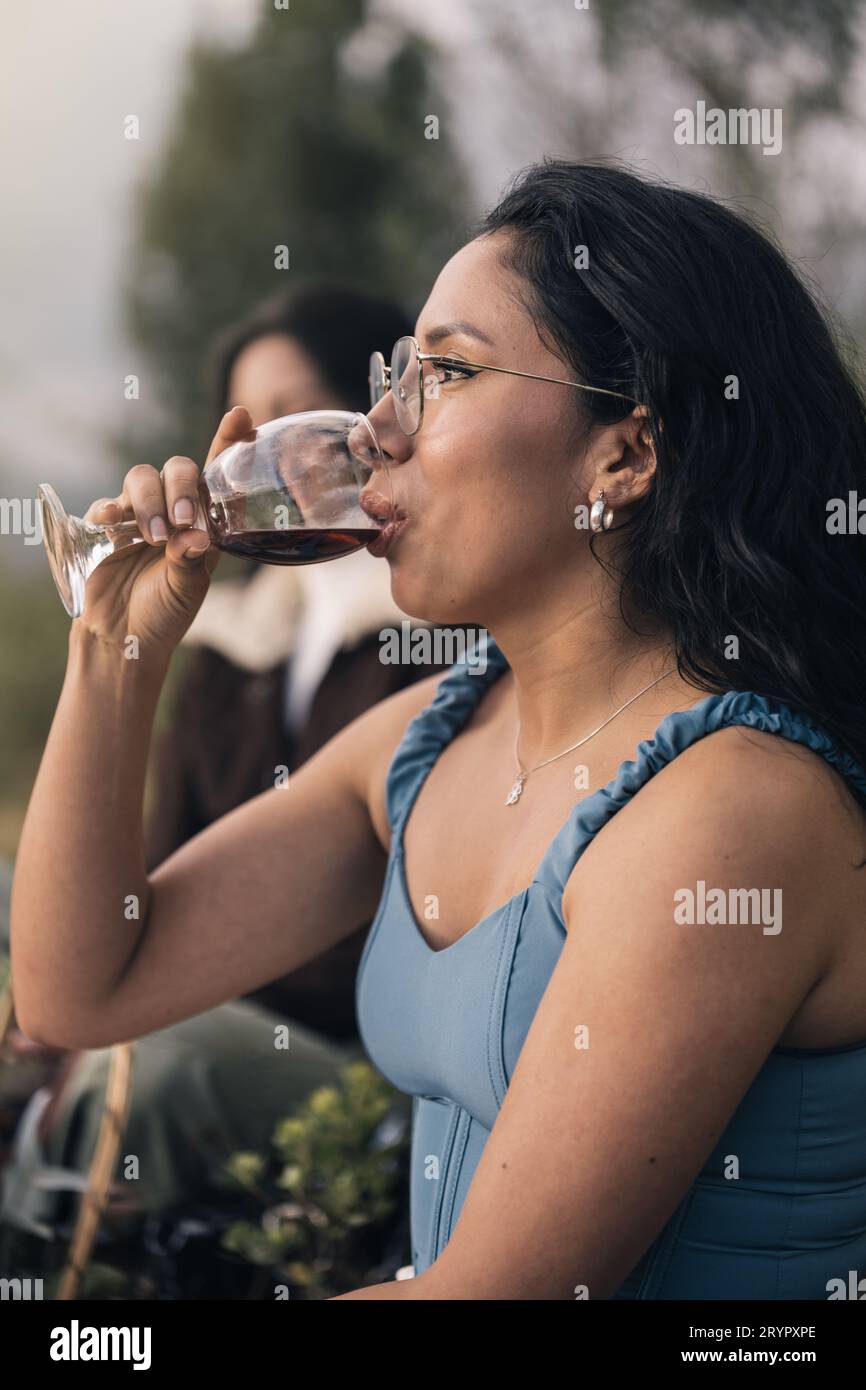 Bella giovane donna ispanica che beve vino rosso all'aperto Foto Stock