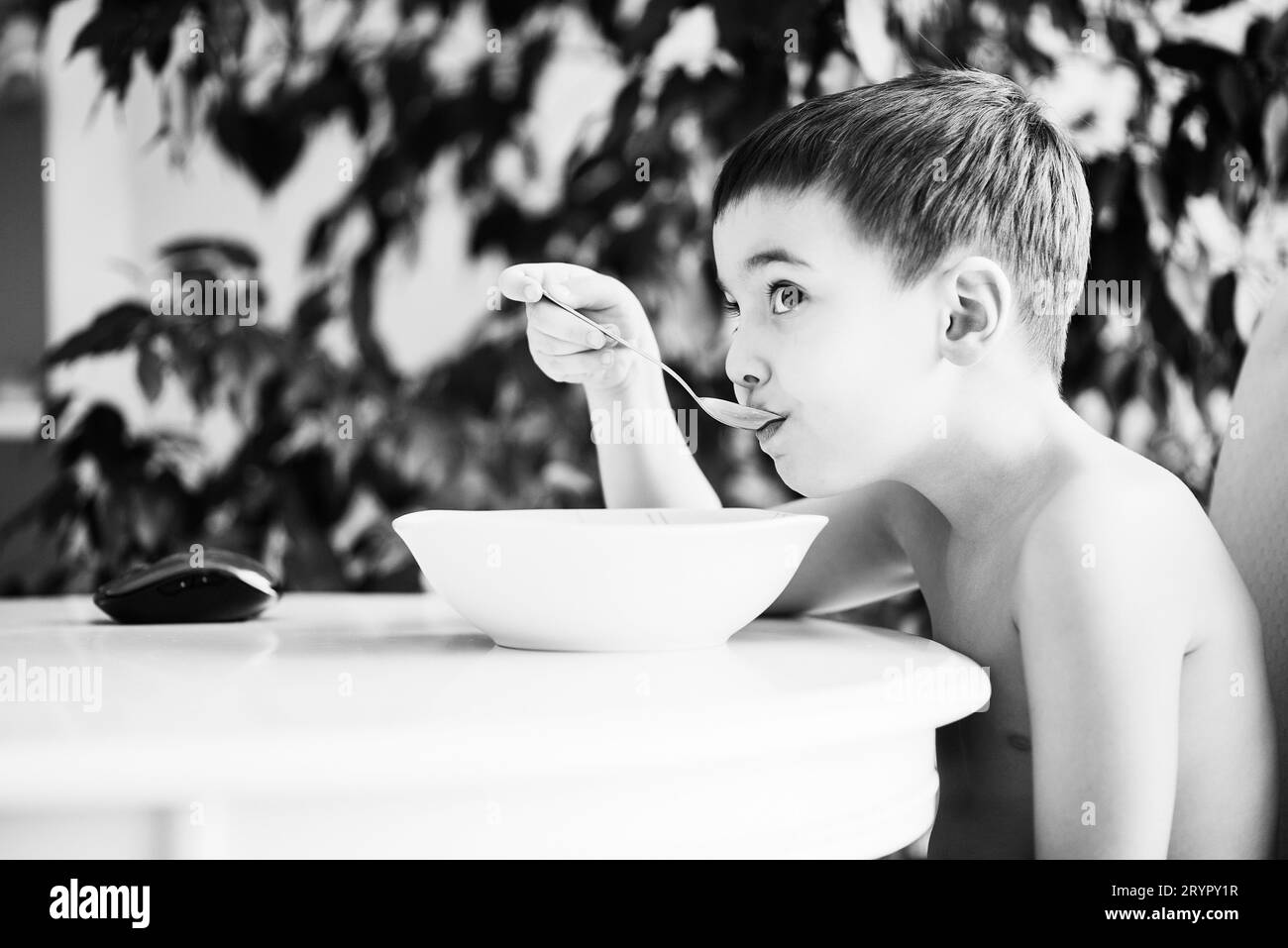 Bambino carino che mangia cibo sano in casa, bianco e nero Foto Stock