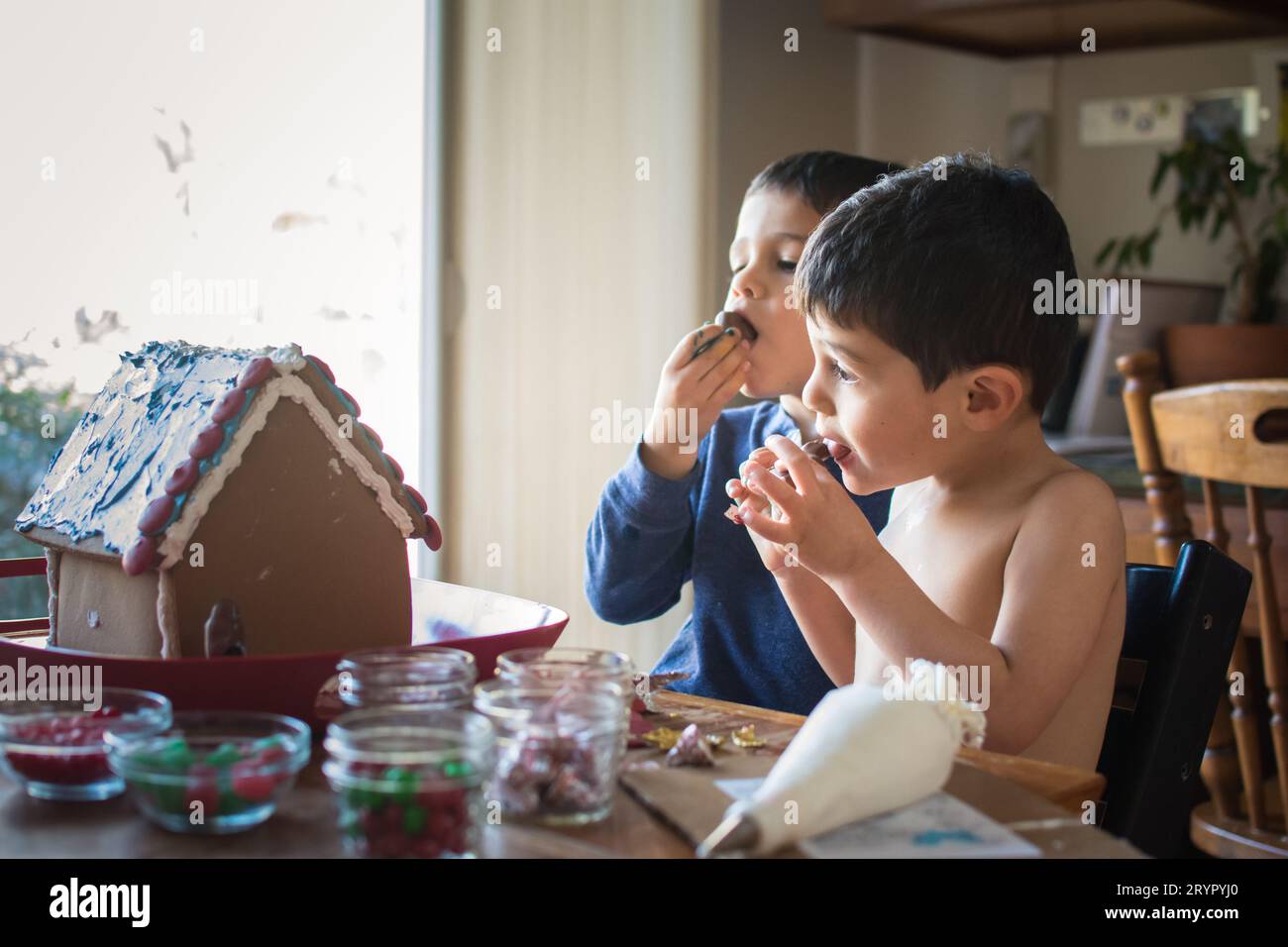 Ragazzi giovani assaggiano caramelle mentre decorano una casa di pan di zenzero. Foto Stock