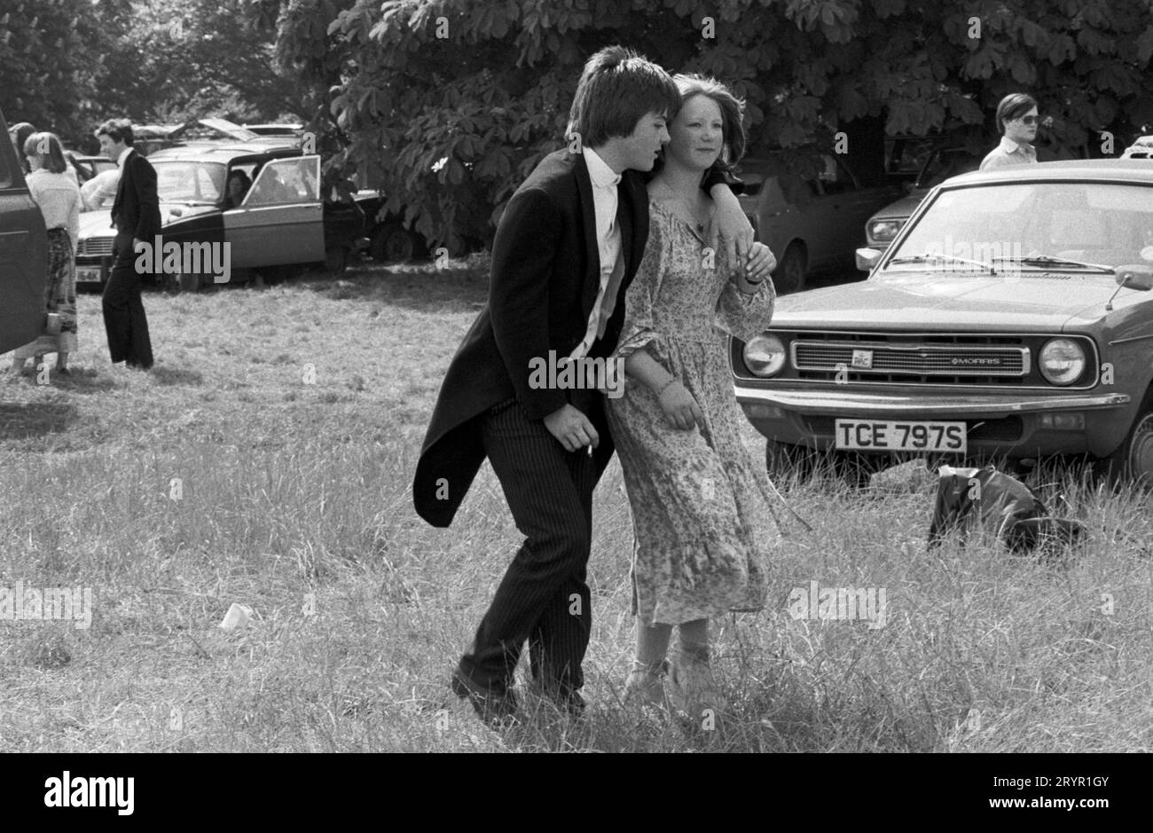 Una coppia studentesca, lo scolaro sta fumando con il braccio intorno alla sua ragazza. Eton College Parents Day, il 4 giugno, le famiglie si riuniscono per un picnic durante la partita di cricket tra le due case. "Intervallo picnic" su Agar's Plough, che è il nome di uno dei campi di gioco appartenenti alla scuola. Eton, Windsor, Berkshire, Inghilterra circa giugno 1978. 1970S UK HOMER SYKES Foto Stock