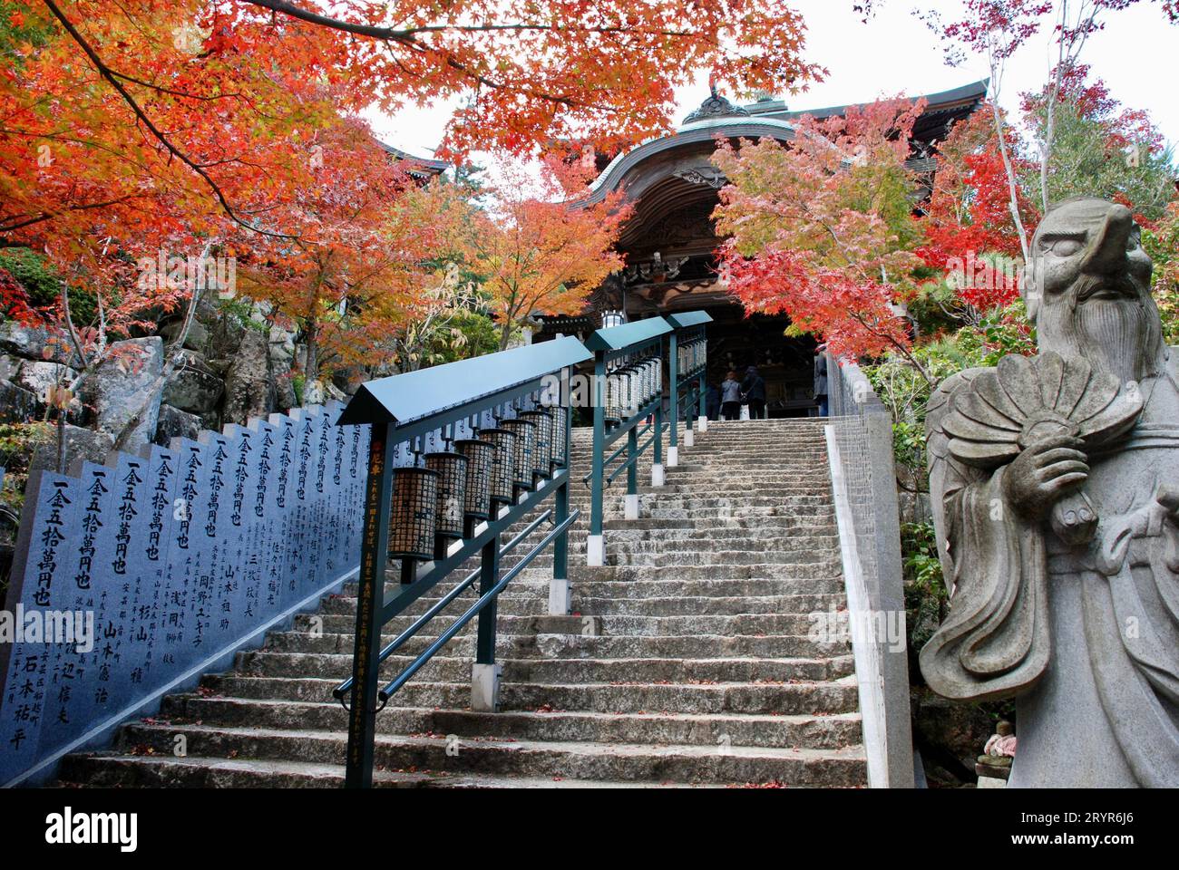 Una maestosa statua in pietra di fronte alle scale in pietra del Tempio di Daishoin, Miyajima Foto Stock