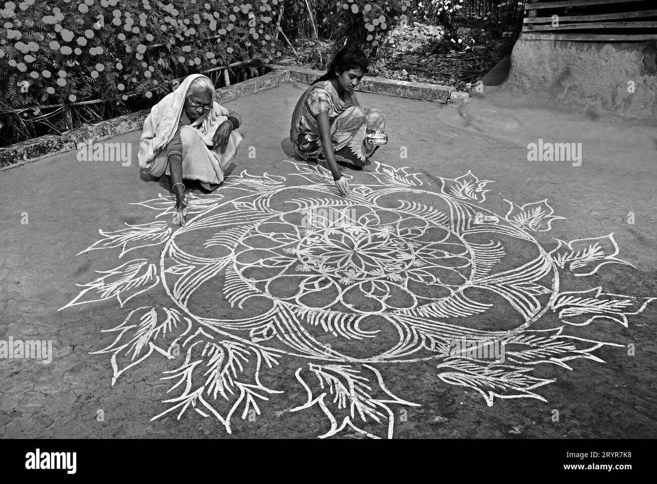 Una vecchia donna e sua nipote disegnano disegni Alpana sul terreno della loro dolce casa nel remoto villaggio di Purulia, nel Bengala Occidentale. Foto Stock