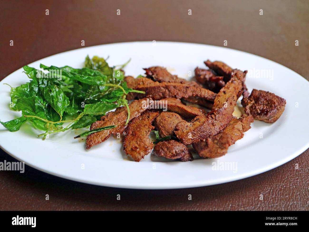 Piatto di fegato di manzo all'aglio alla griglia servito con basilico croccante fritto Foto Stock